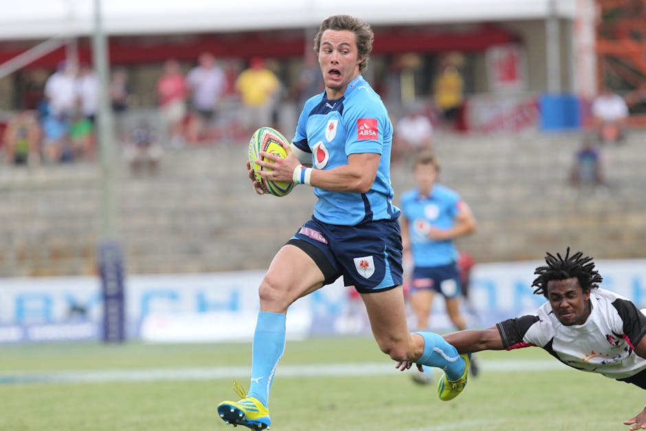 Intense rugby match showing players running with ball on field, avoiding tackle.