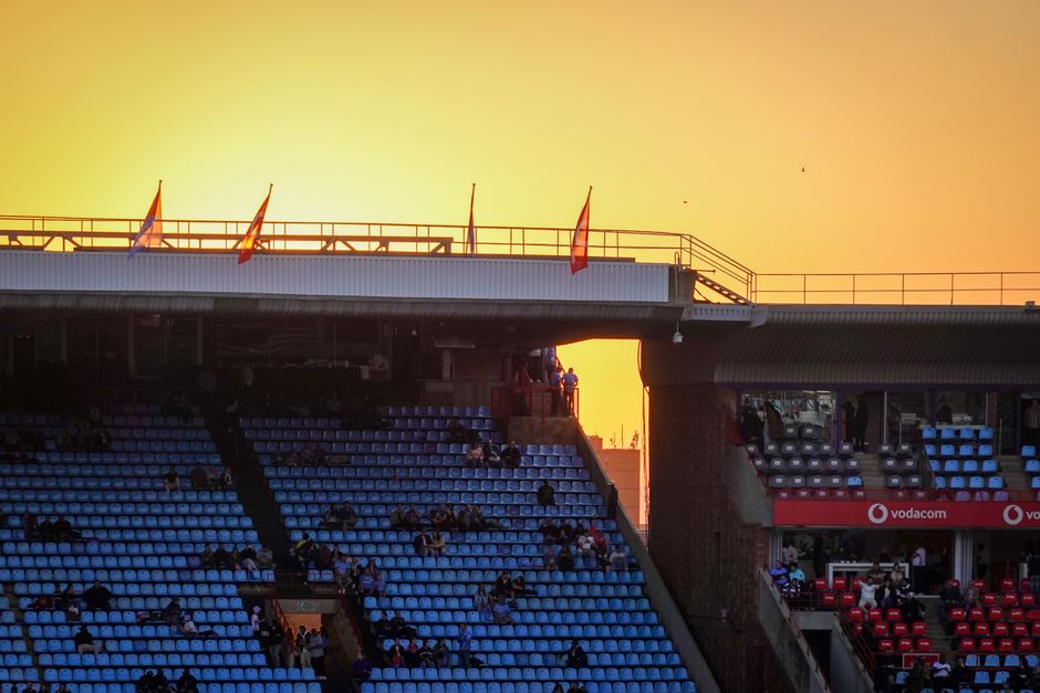 A vibrant sunset over a rugby stadium with blue and red seating, creating a warm ambiance.