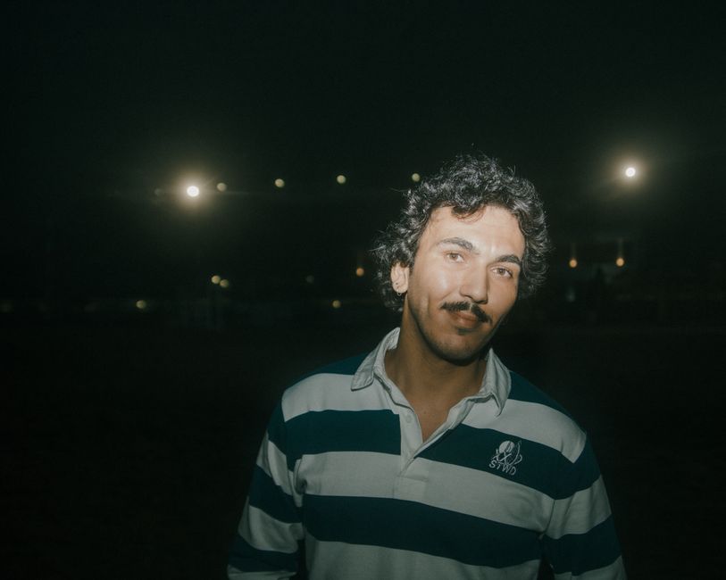 Portrait of a man with curly hair and mustache illuminated at night, adding depth to the scene.